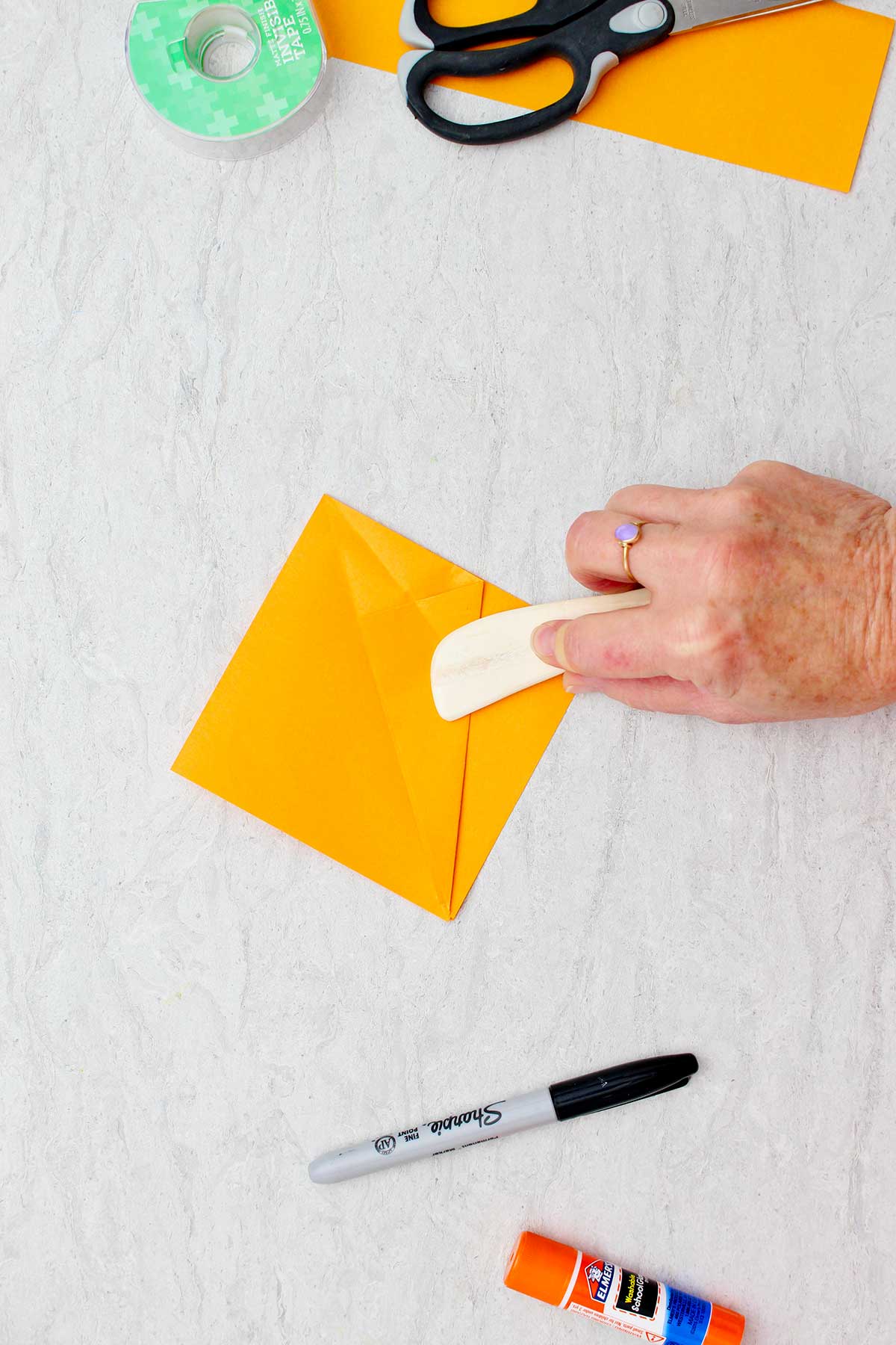 Person using rounded wooden stick to sharpen folded edges on an orange piece of paper used to make an origami pumpkin.