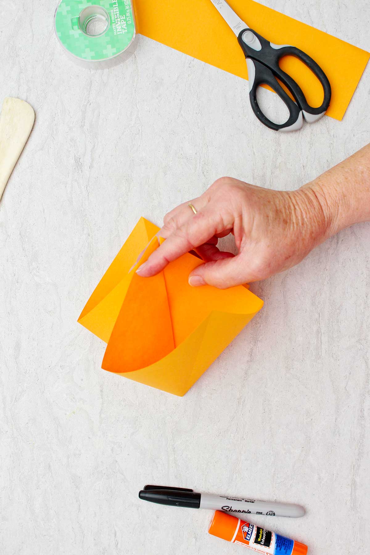 Person showing inside view of folded orange paper to make an origami pumpkin.