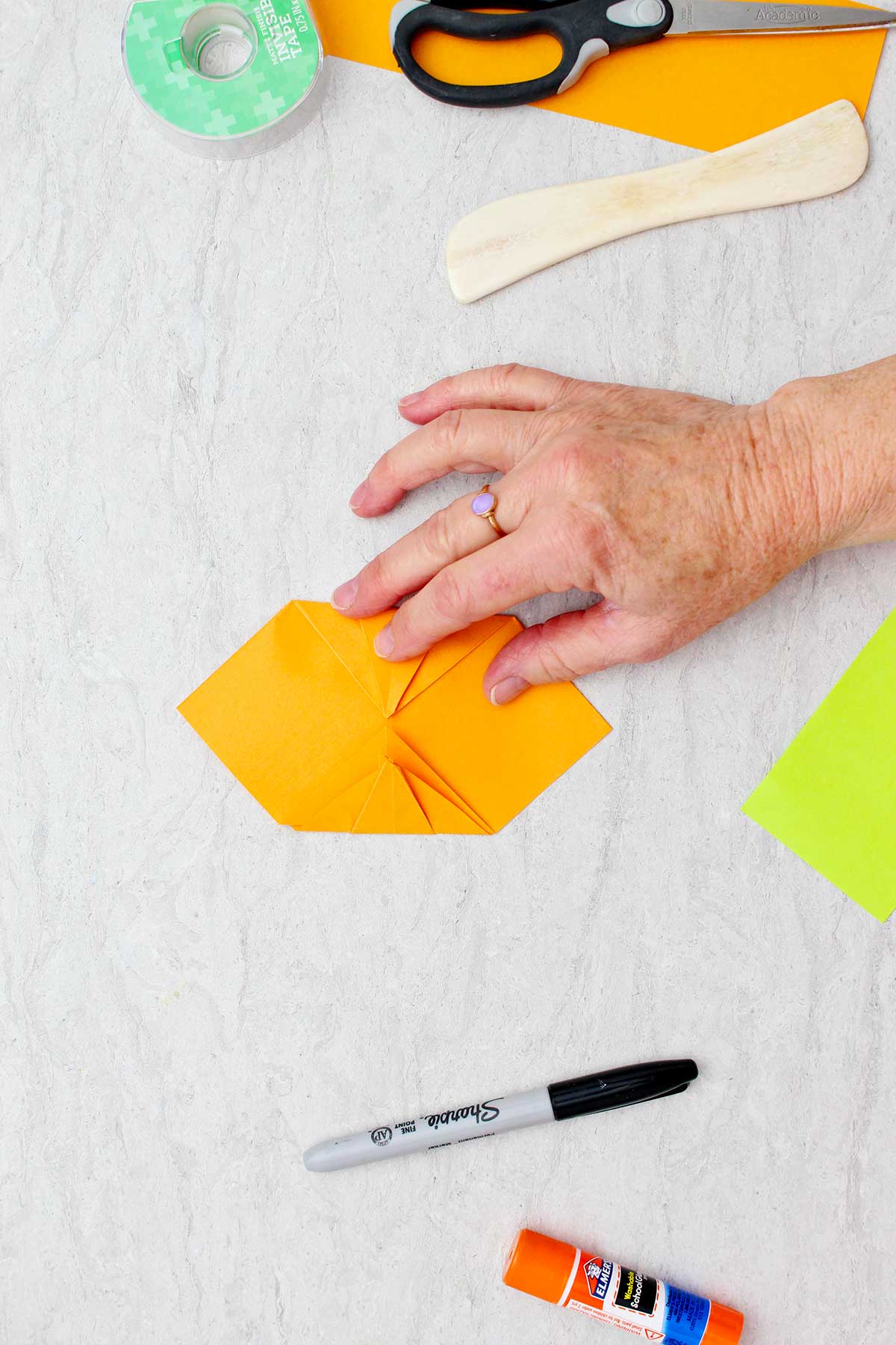 Person folding two folded sides in towards each other to create an origami pumpkin.