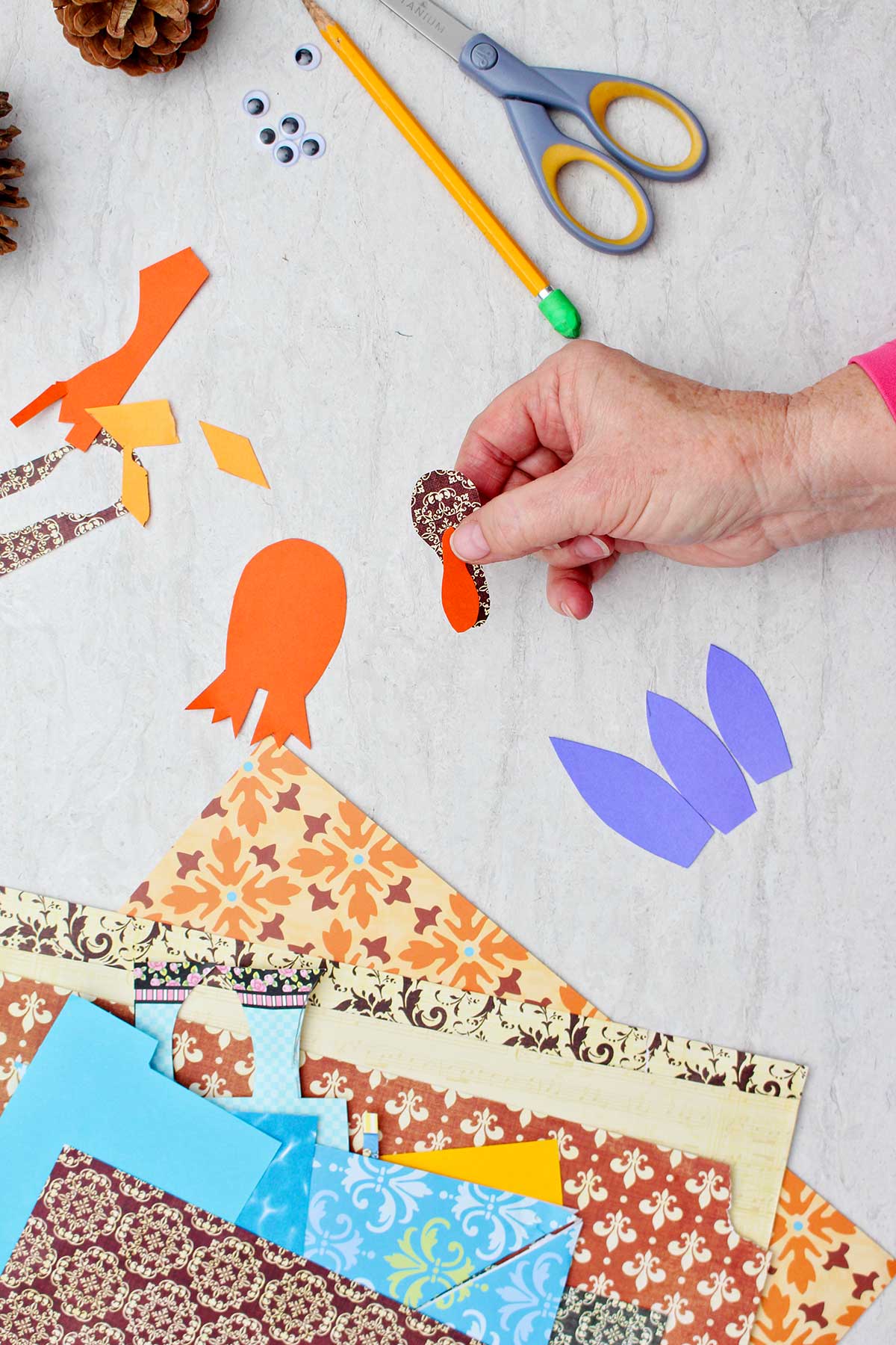 Person gluing a red piece of paper to brown one to make a turkey head with other supplies near by.