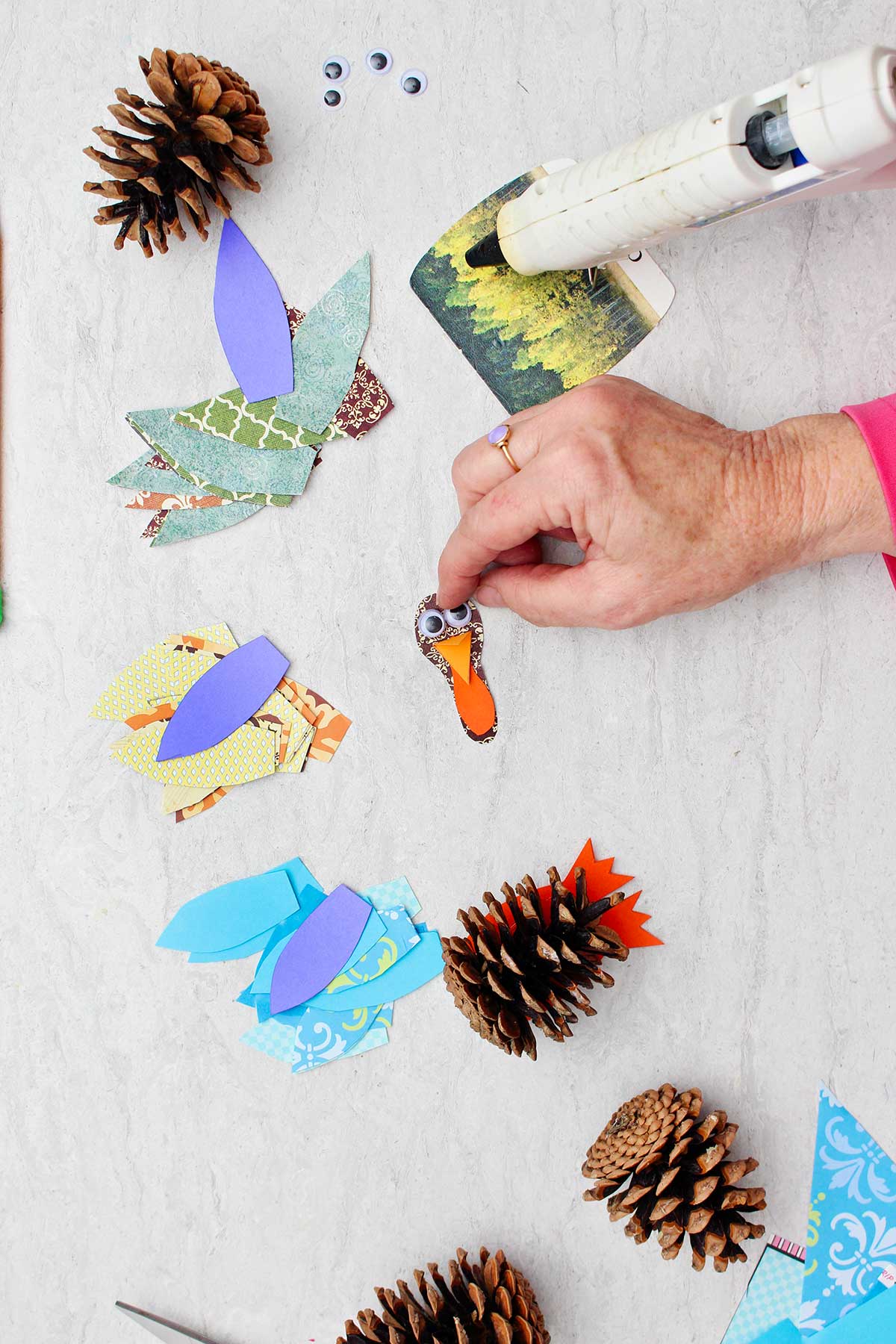 Person gluing google eye on a brown piece of scrapbook paper to make a turkey face with other supplies near by.