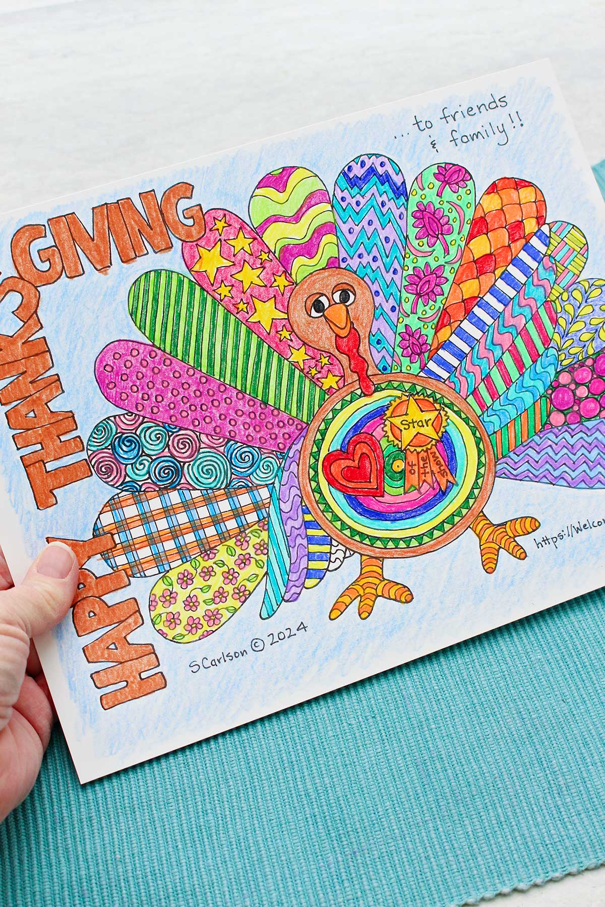 A person holding a Thanksgiving coloring page saying "Happy Thanksgiving" and a turkey with colorful patterned wings.