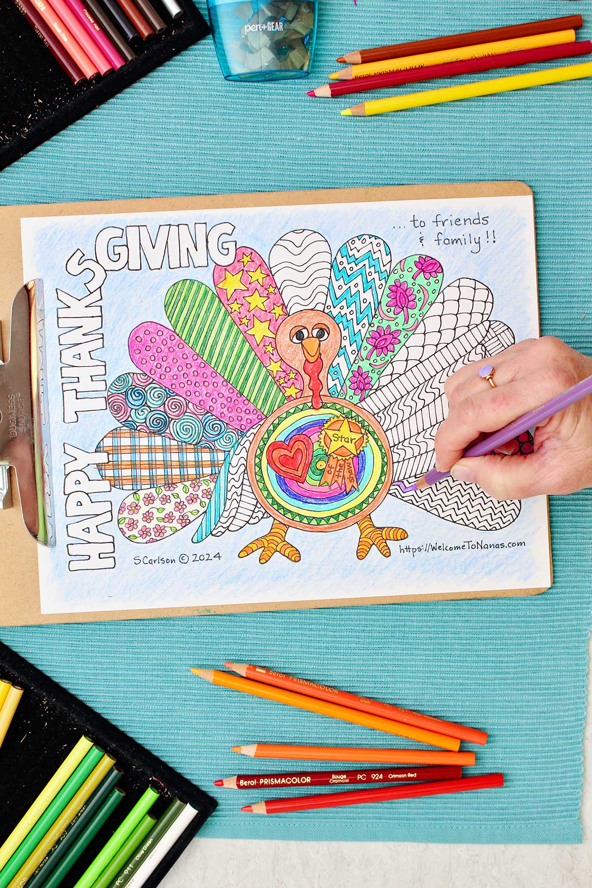 Thanksgiving coloring page of a turkey with patterned wings is clipped into a clipboard and resting on an aqua placemat with colored pencils near by. Person coloring in feather purple.