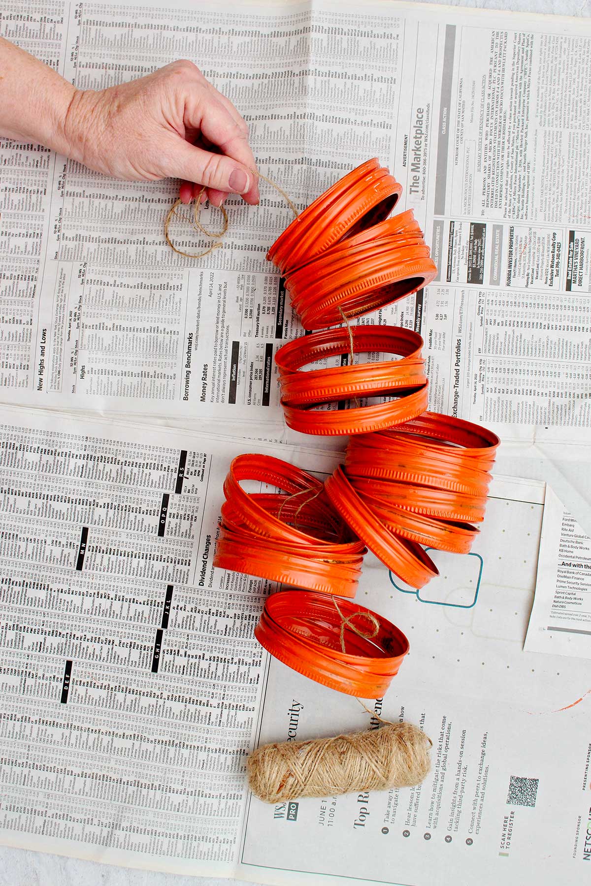 Person stringing a piece of twine through all 20 painted mason jar lids.