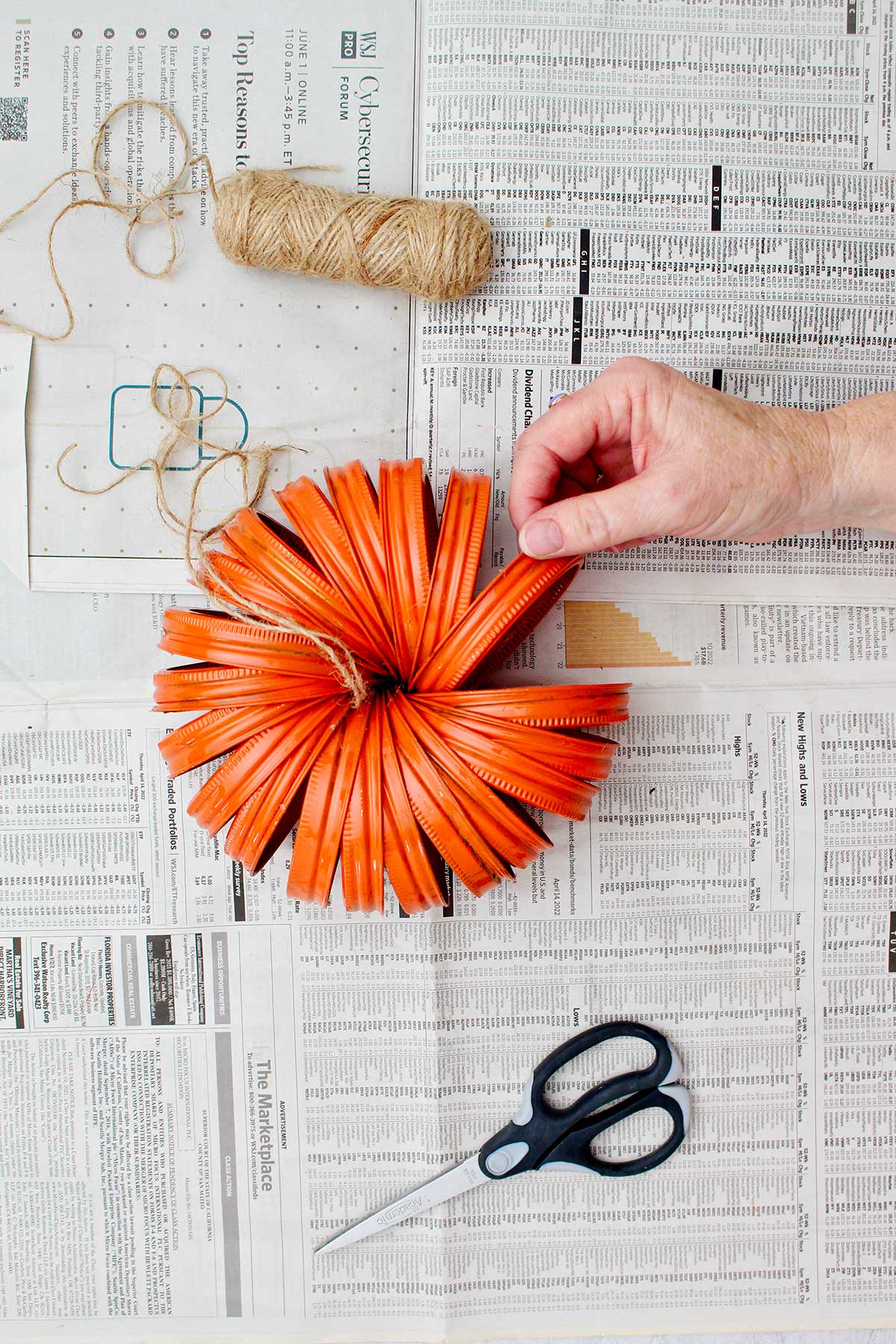 Person adjusting and fanning out tied up mason jar lids with extra twine and black scissors near by.