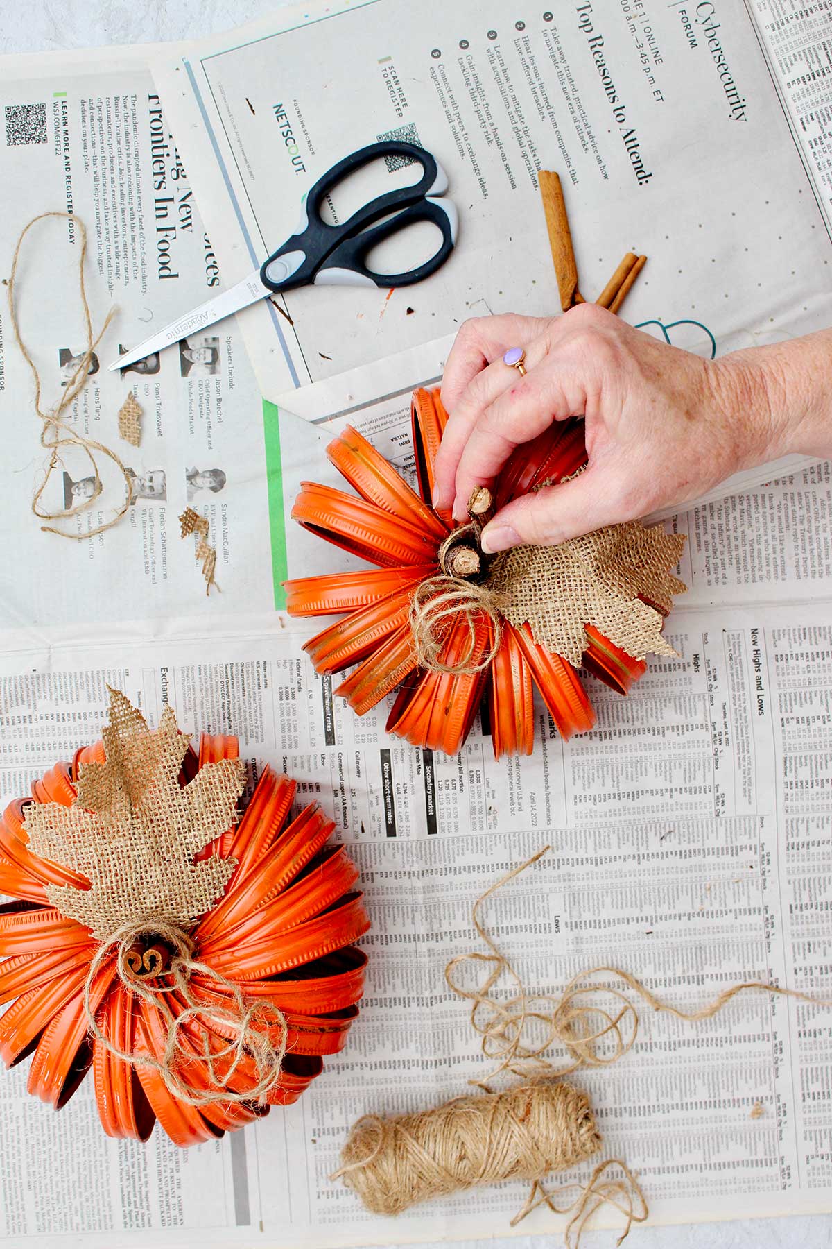 Person adjusting stick in center of second pumpkin for a stem with other supplies and finished pumpkin near by.