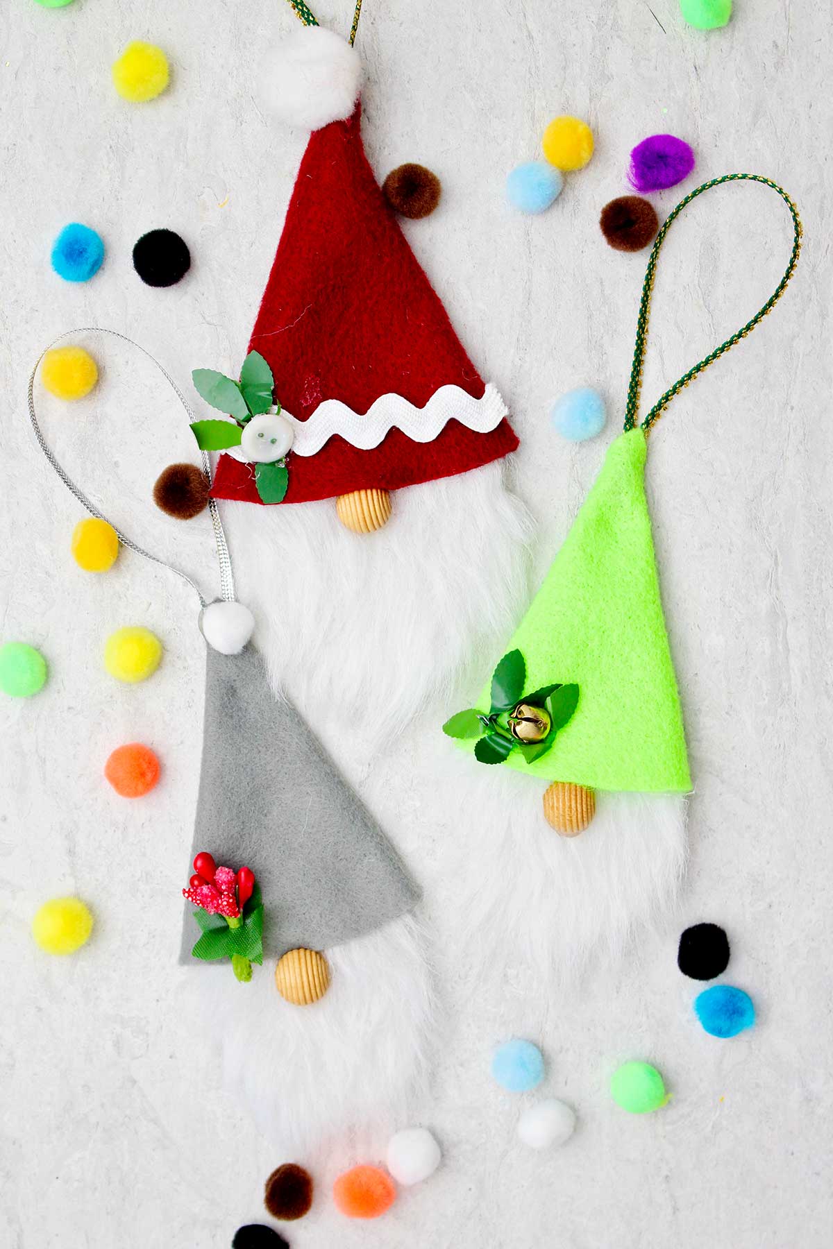 Three completed gnome Christmas ornaments with colorful pom poms scattered around.