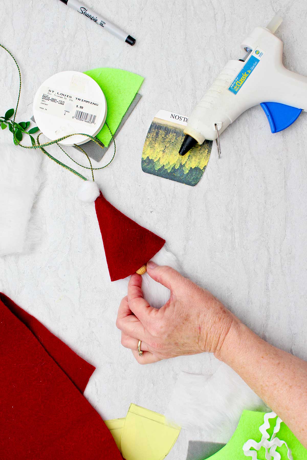 Person adding a wooden bead as a nose to a gnome Christmas ornament with other supplies near by.