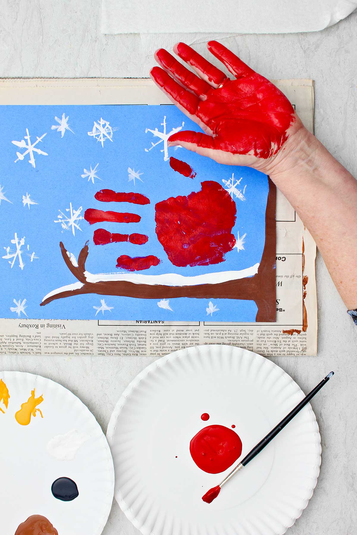 Person showing their red painted hand after stamping it on their winter scene construction paper.