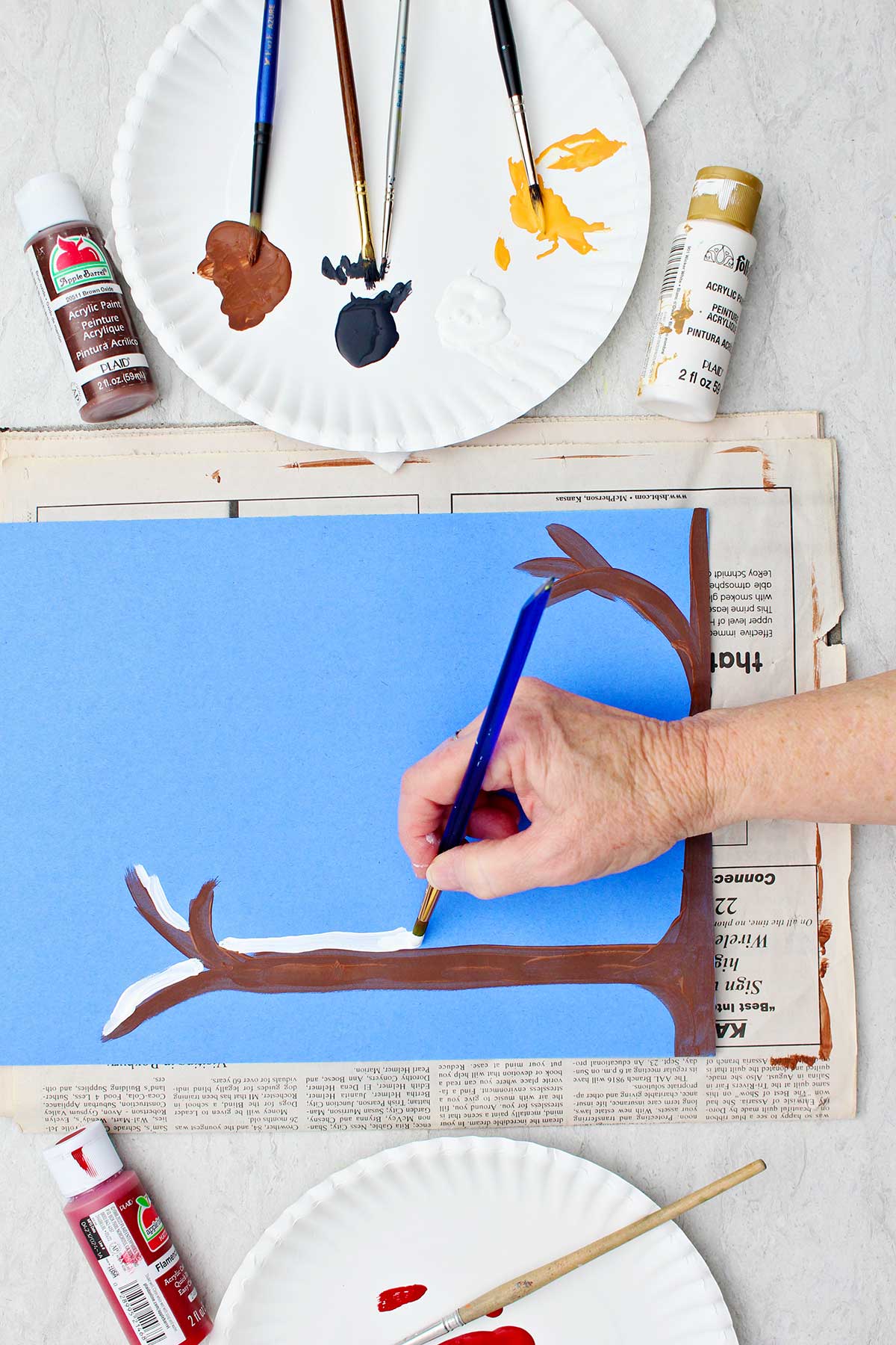 Person adding snow on top of a branch in their winter scene on blue construction paper.