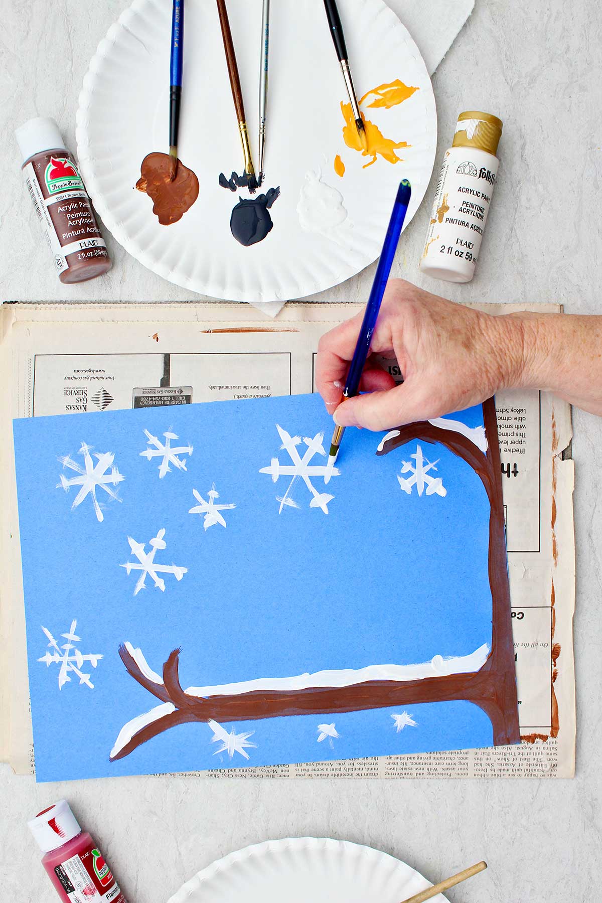 Person adding white snowflake details to their winter scene on blue construction paper.