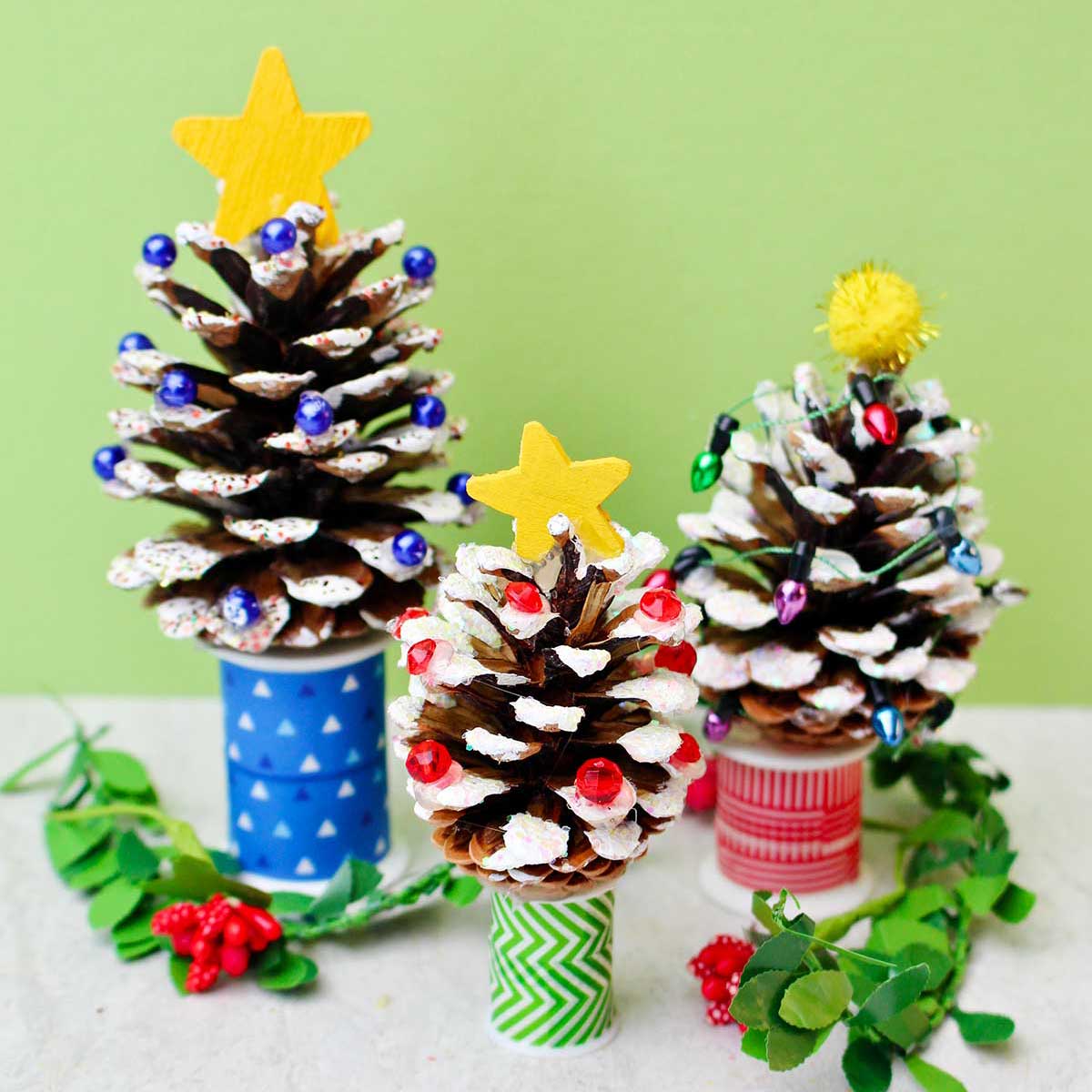 Three painted DIY Pinecone Christmas Trees with stars and bead lights