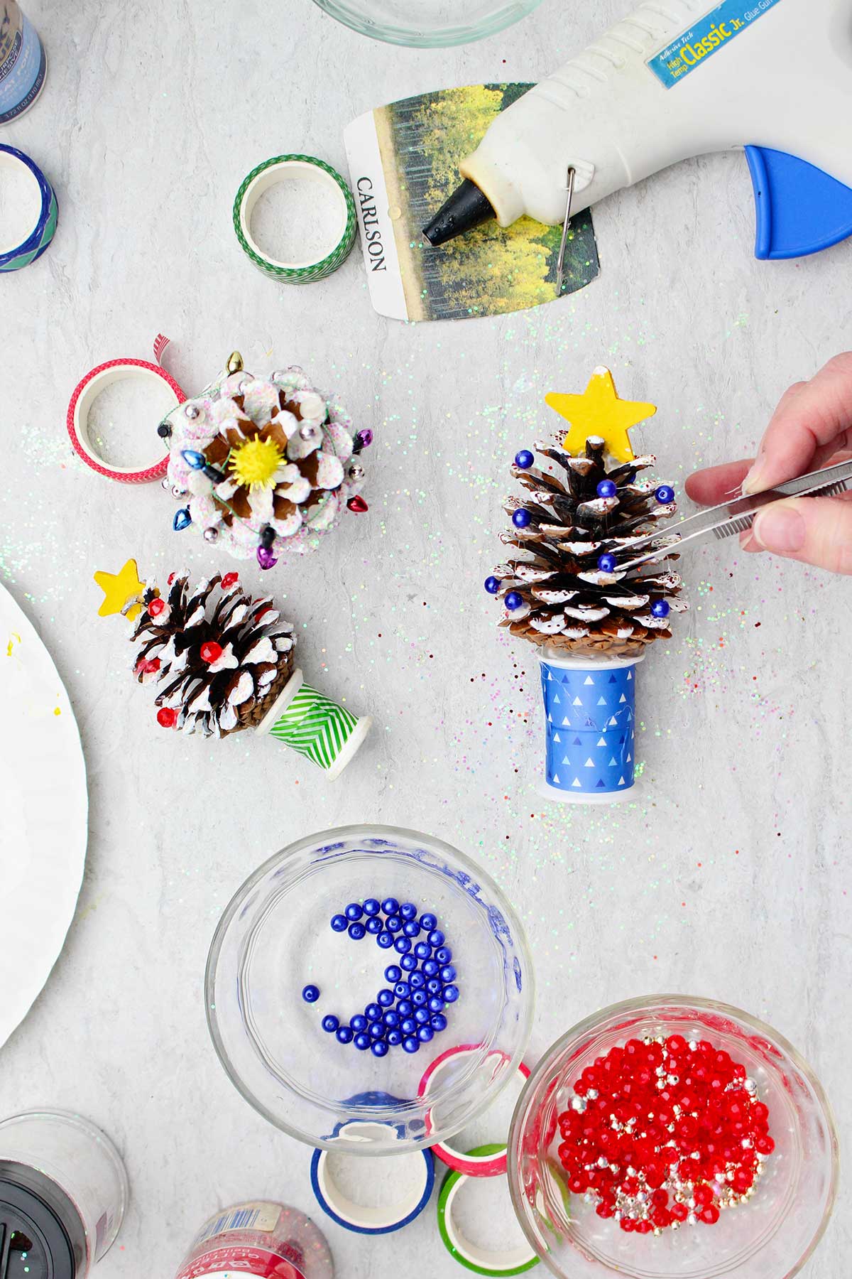 Adding bead "lights" with tweezers to a painted Pinecone Christmas Tree