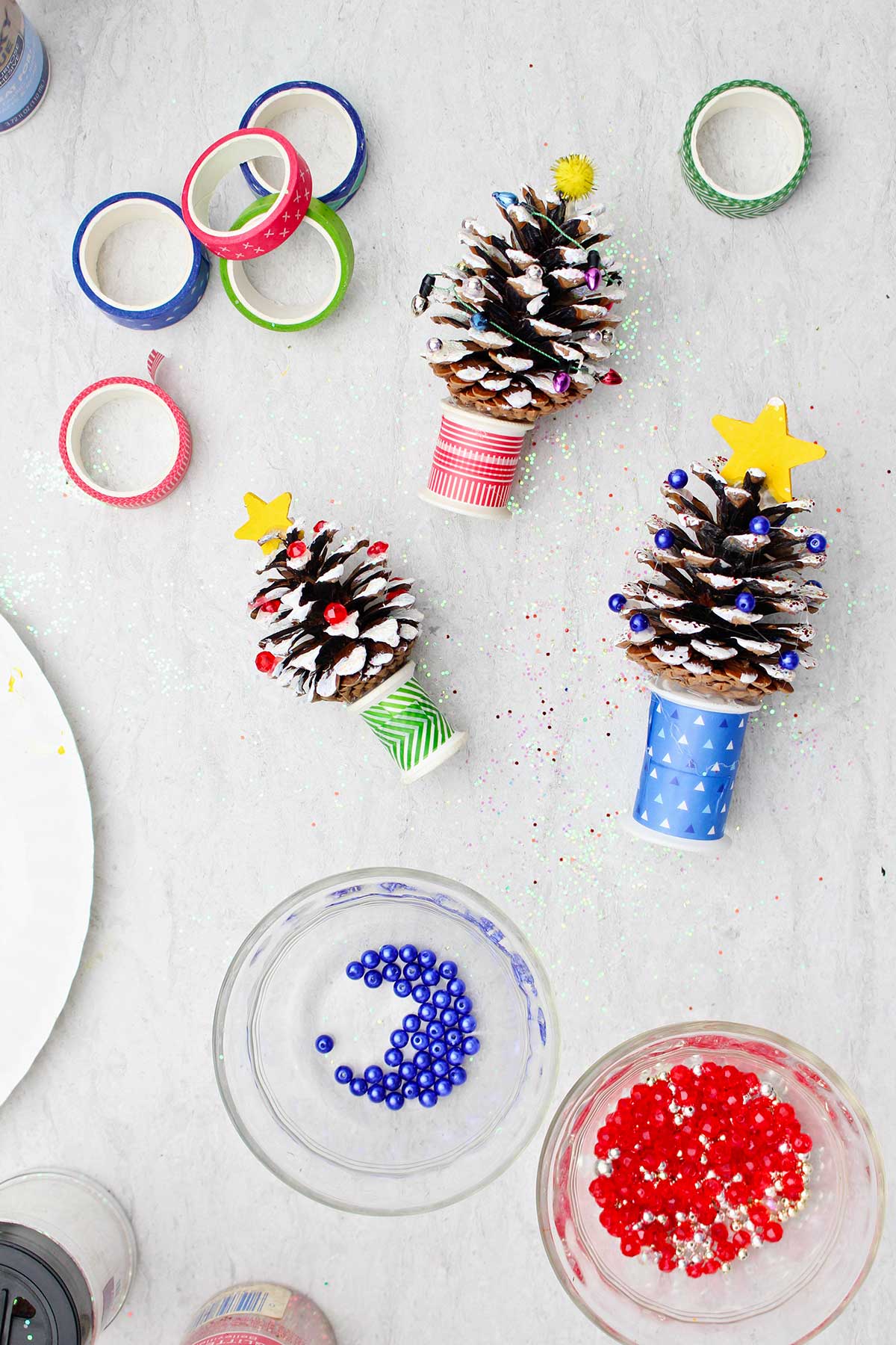 Three painted DIY Pinecone Christmas Trees with stars and beads ready to add as "lights".