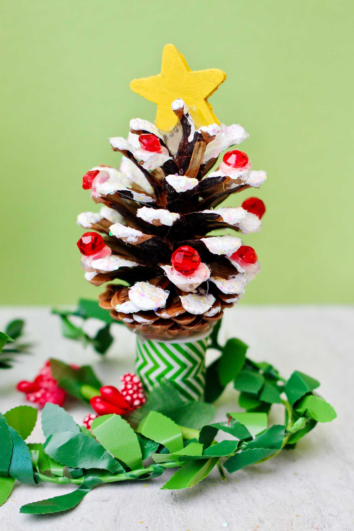 A pinecone painted with white "snow", decorated with red beads, glitter, and a painted yellow star to look like a Christmas tree