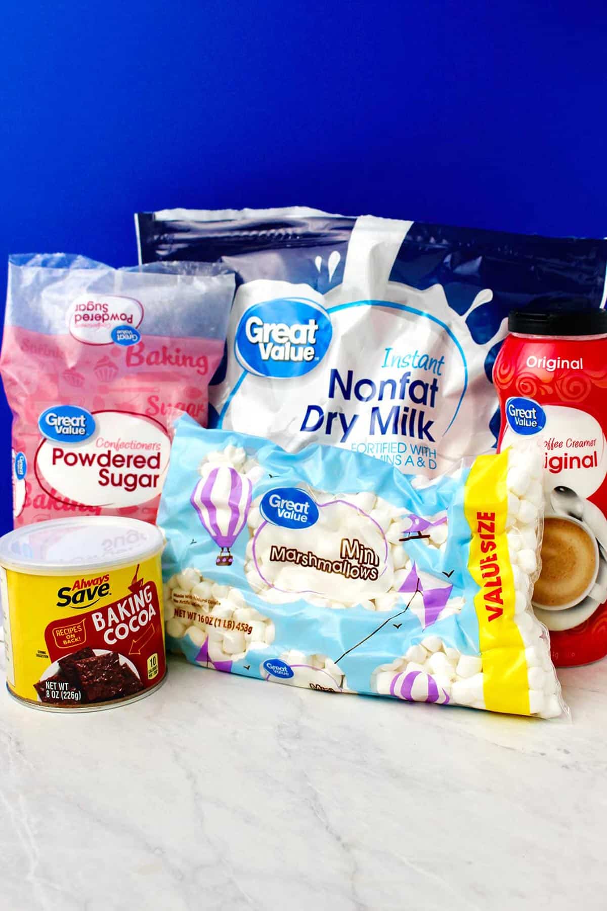 Supplies for hot chocolate mix on a counter against a royal blue background.