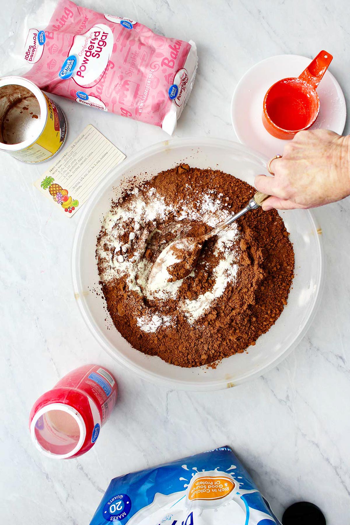 Hand stirring hot chocolate mix in bowl with supplies near by.