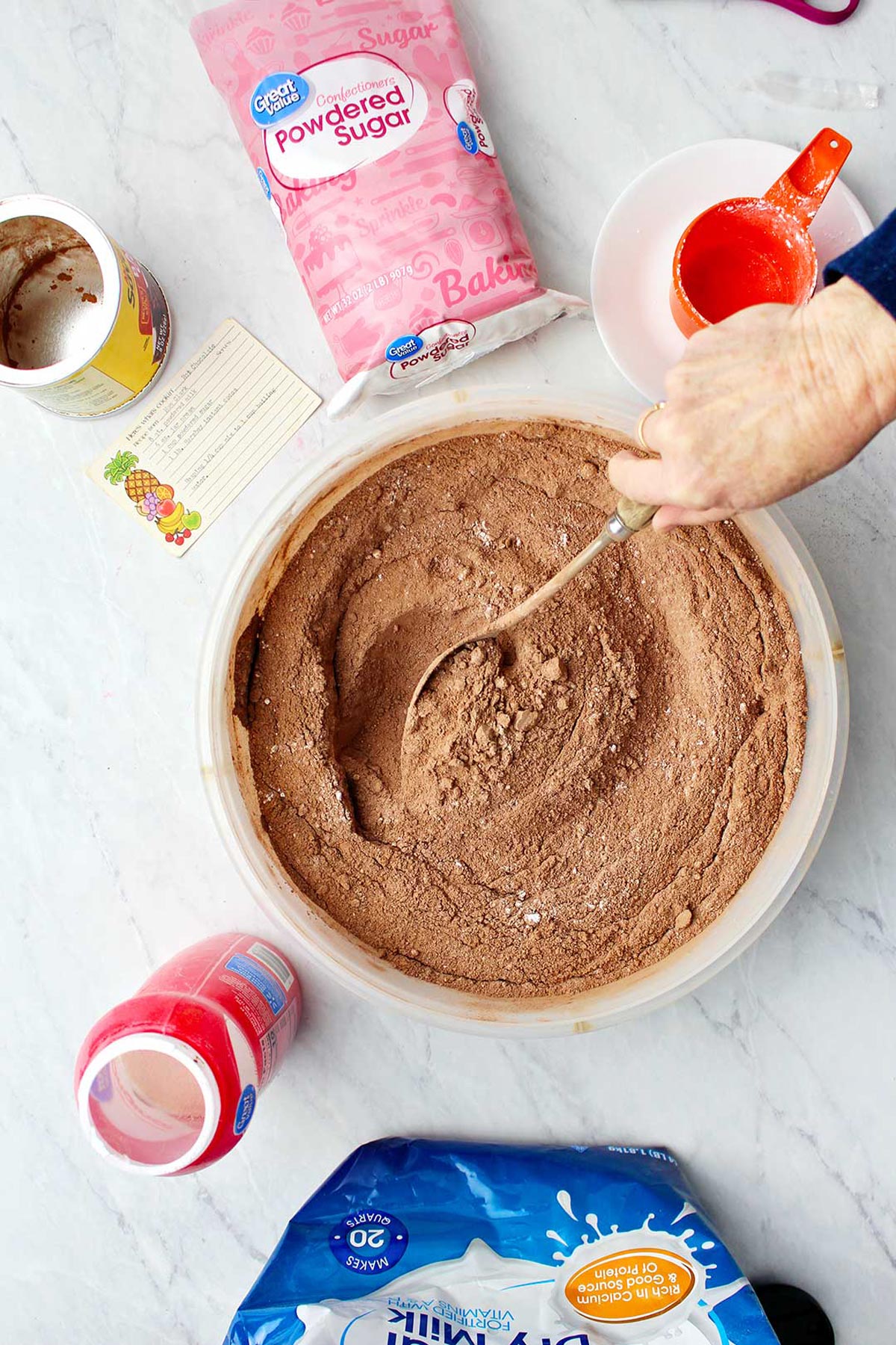 Hand stirring hot chocolate mix in bowl with supplies near by.