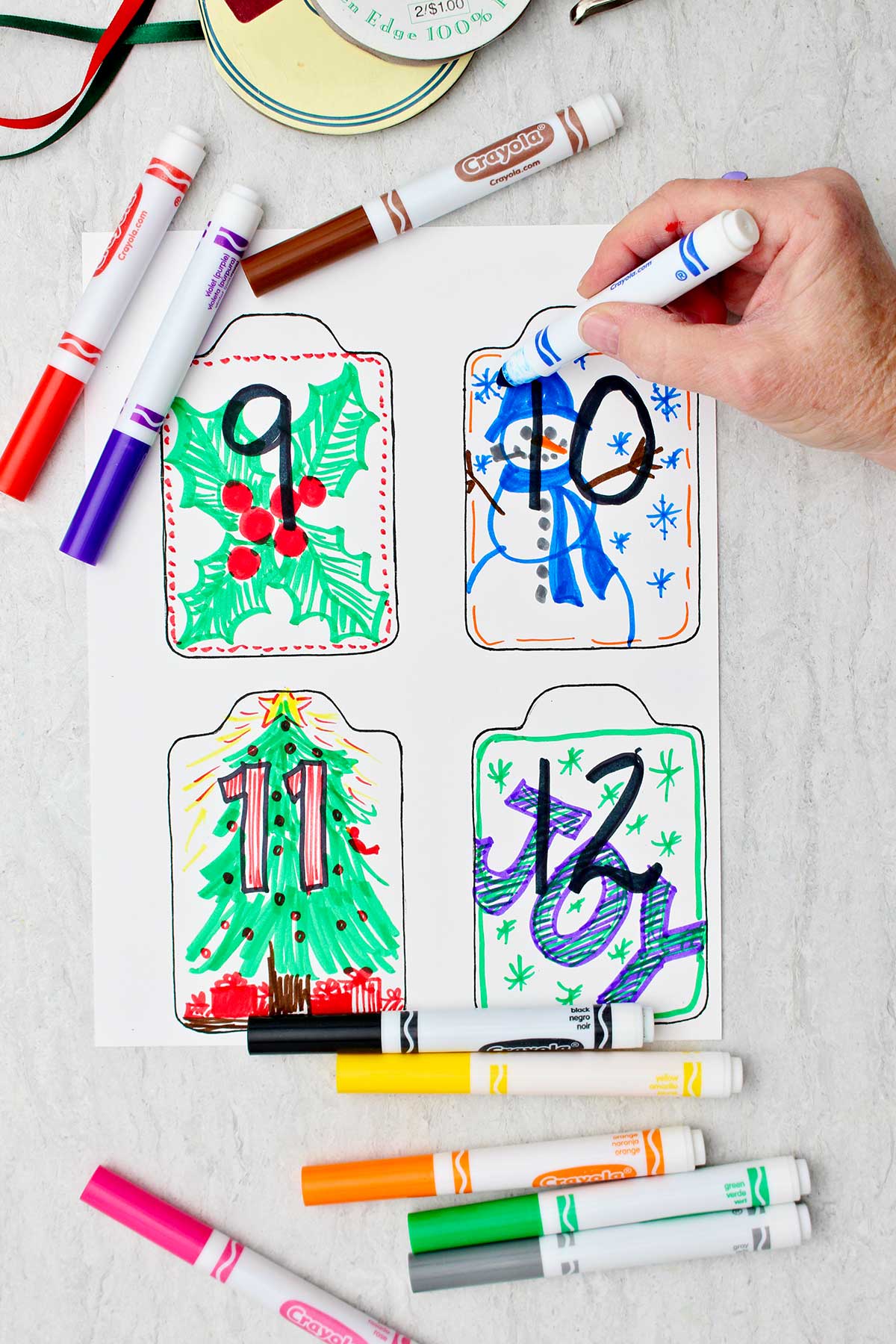 A person coloring a snowman on card number 10 with other completed cards ready to be cut out.