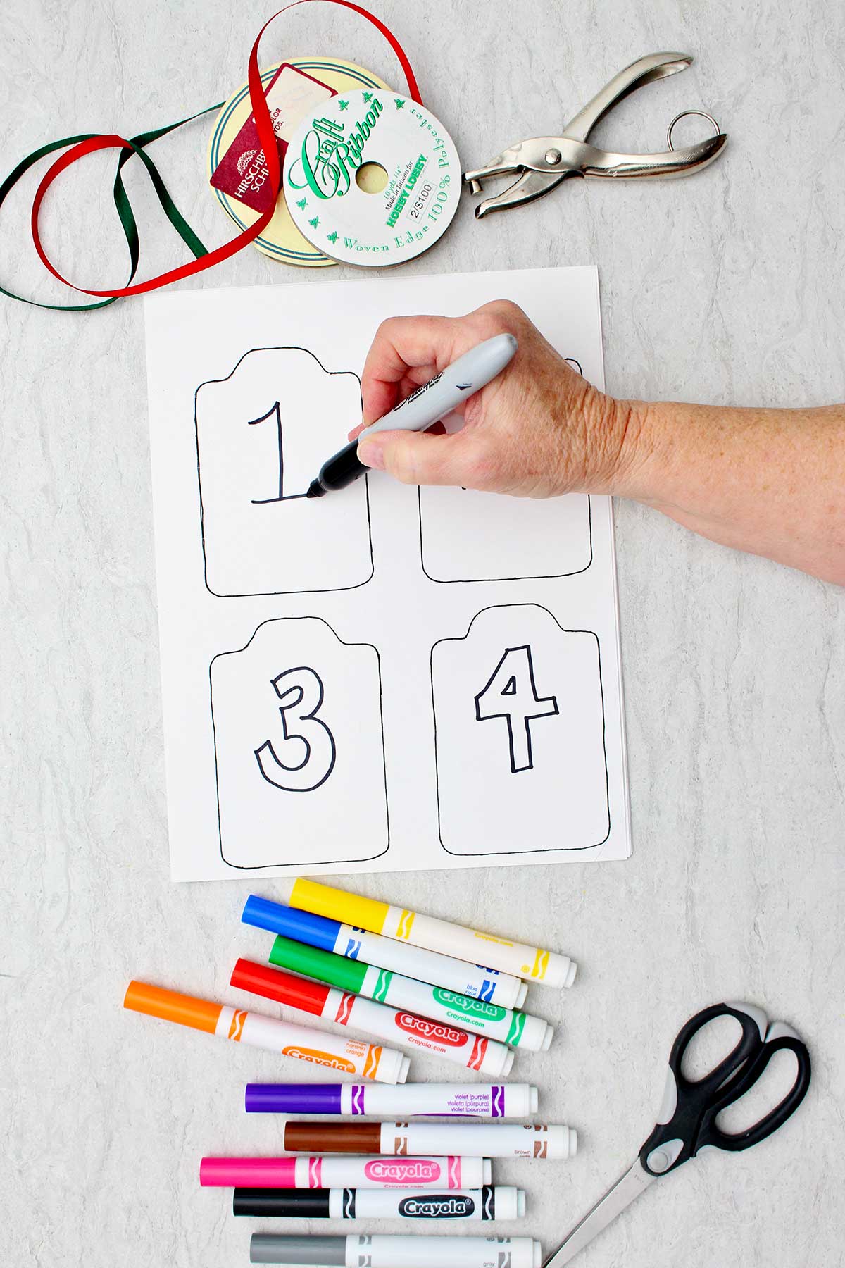 Person numbering blank printed kindness cards with a sharpie marker with other colorful markers and supplies near by.