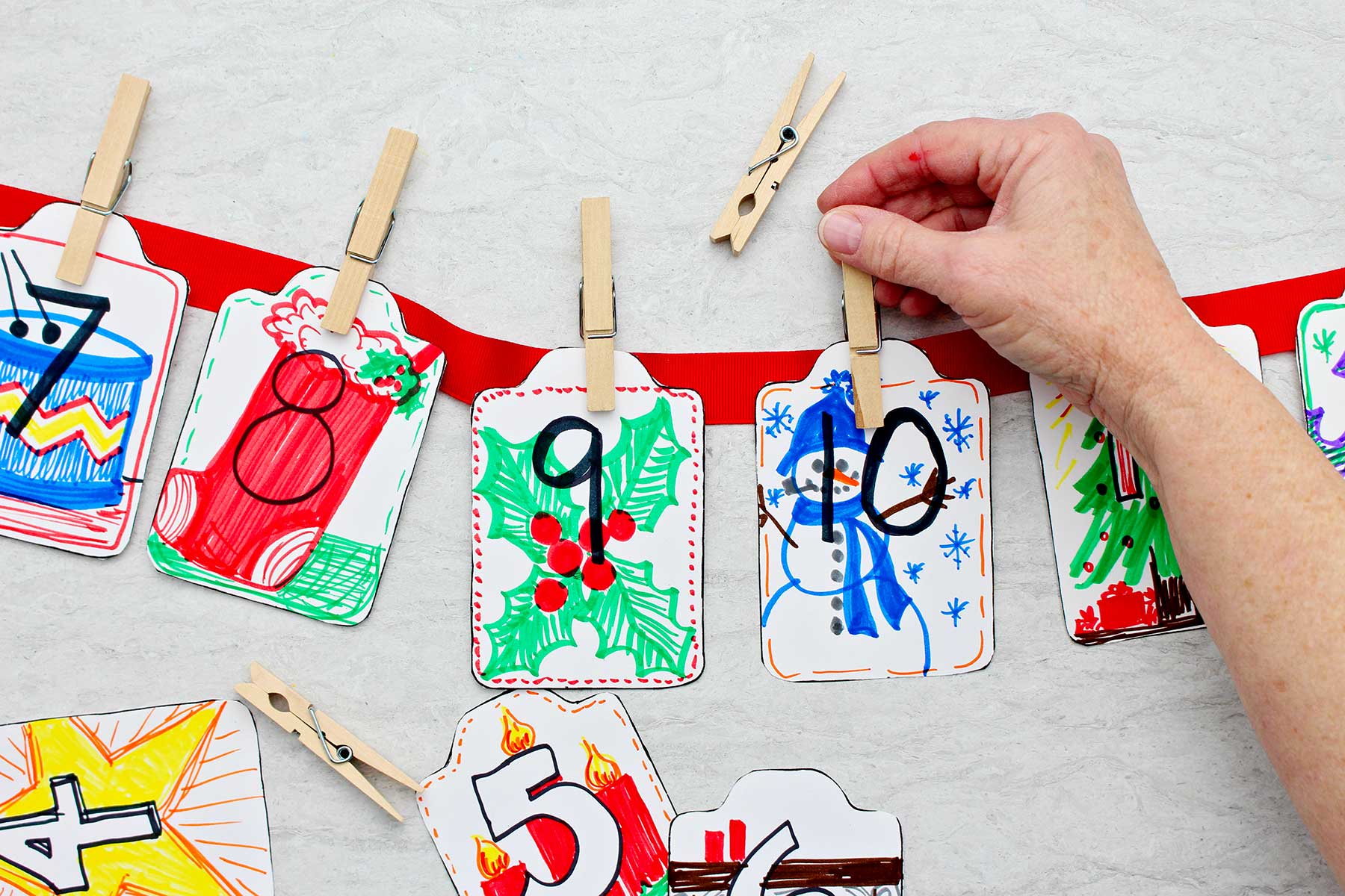 Person clipping kindness card number ten on to a red ribbon with other cars clipped to it.