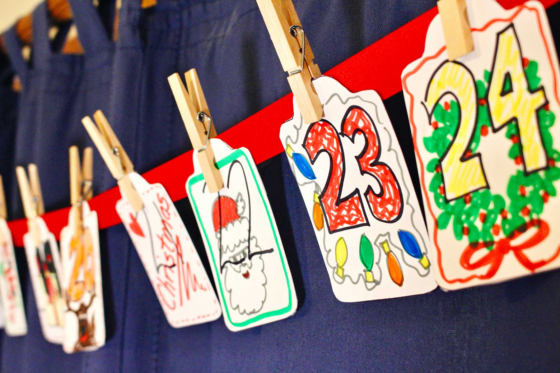 Angled shot of cards 19-34 clipped to a red ribbon with festive, colorful drawings on them.