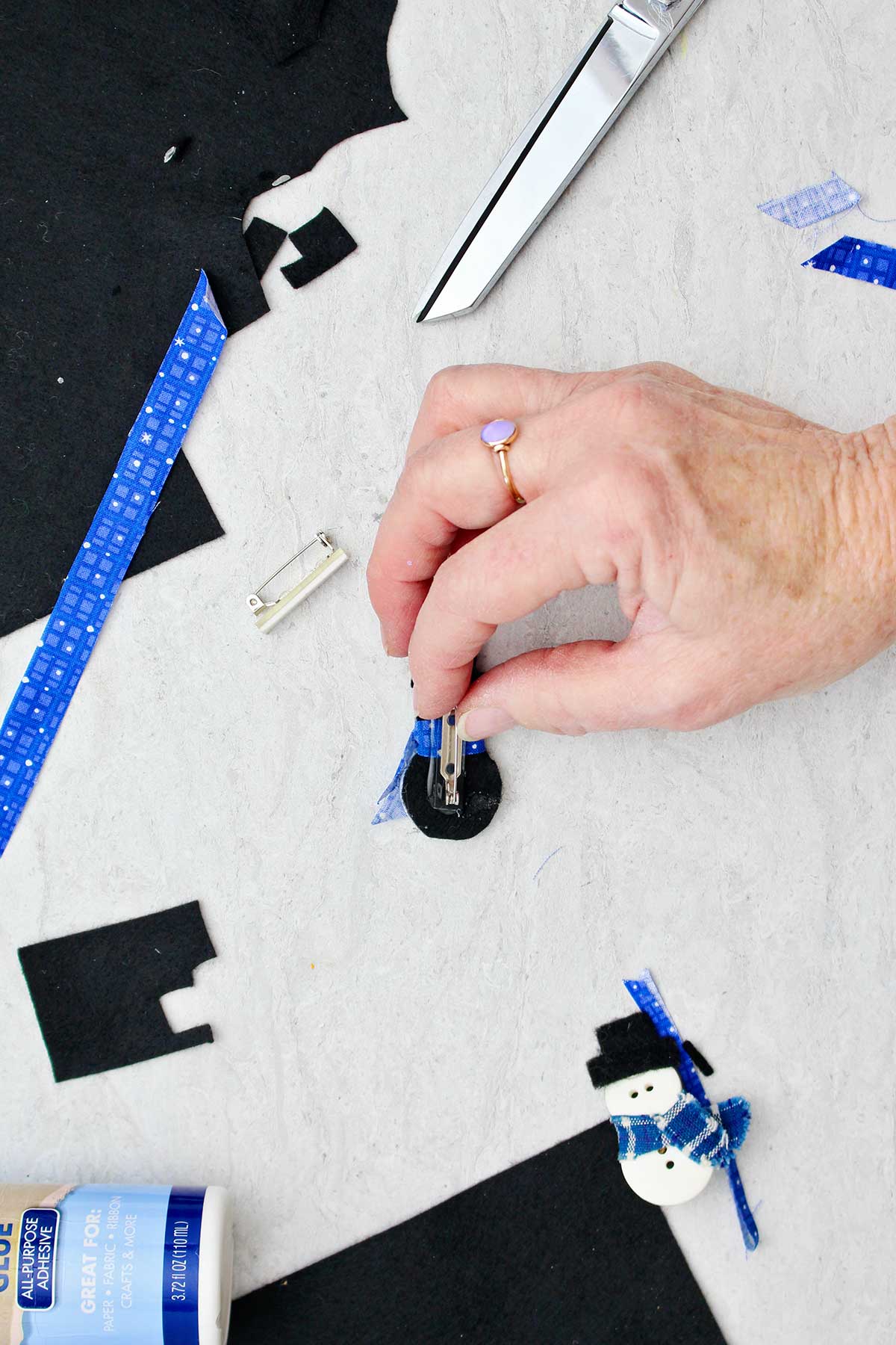 Person adding a pin to the back of a button snowman with scraps of fabric near by.