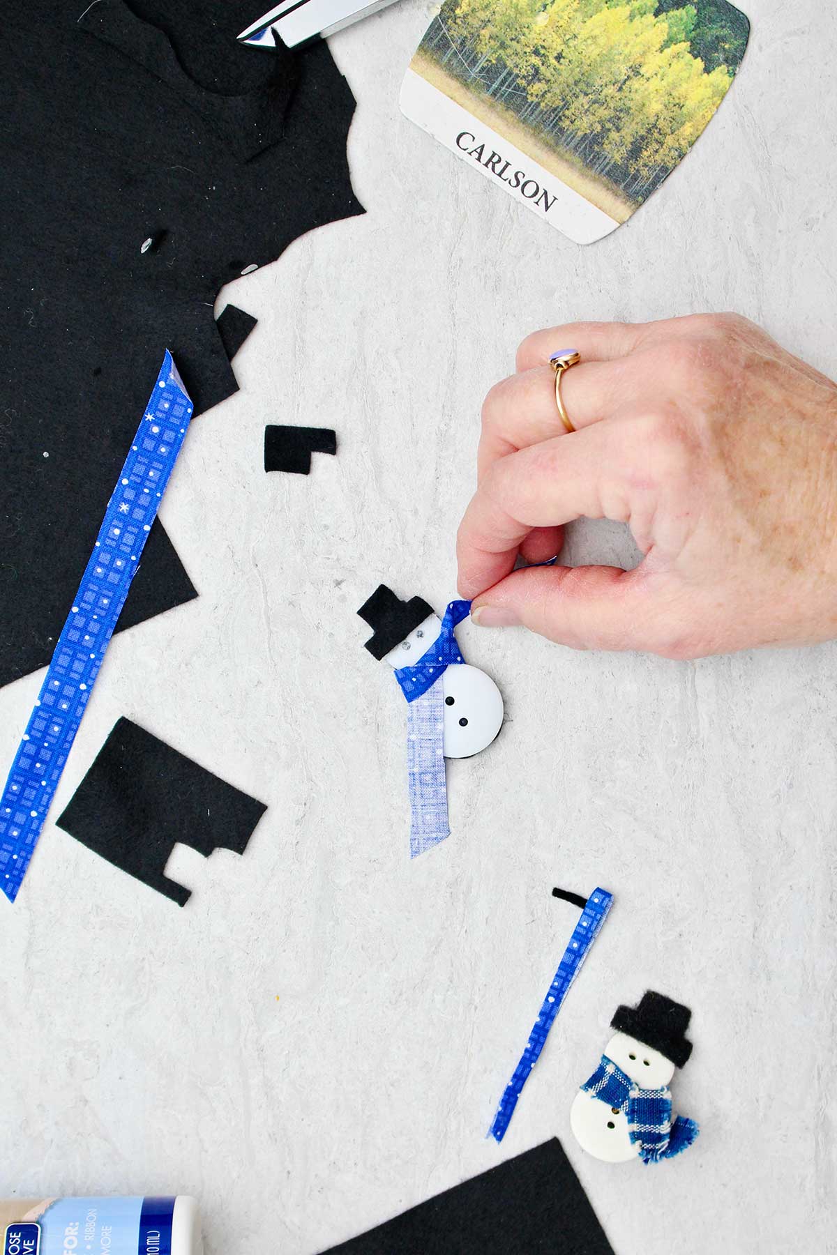 Person adding scarf detail to button snowman with scraps of fabric near by.