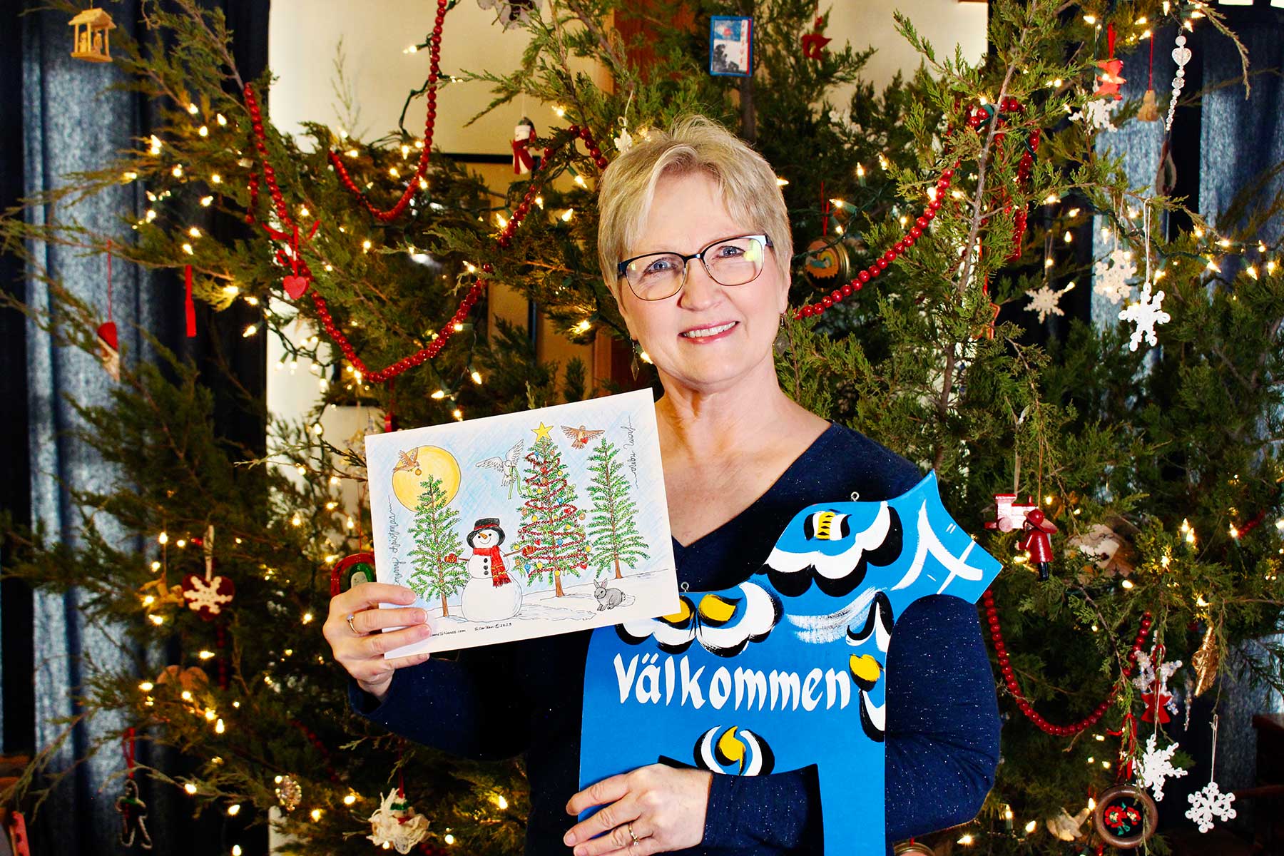 Photo of Nana holding a completed Christmas tree coloring page in front of her Christmas tree.