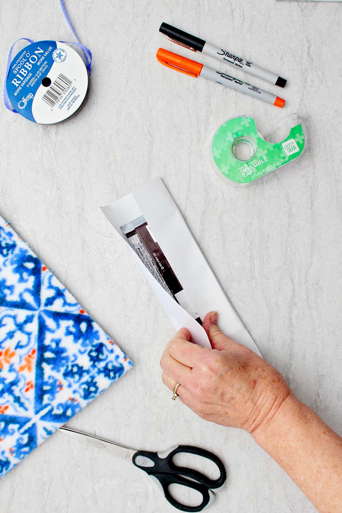 Person wrapping a candy bar in white paper with other supplies to make snowman stocking stuffer near by.