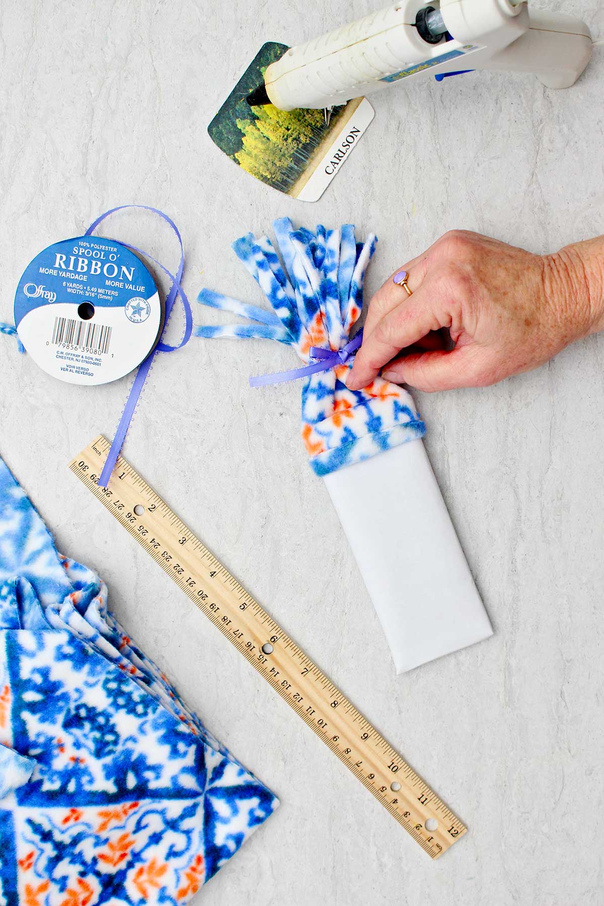 Person securing fleece hat on top of the white paper wrapped candy bar to make snowman with other supplies to make snowman stocking stuffer near by.