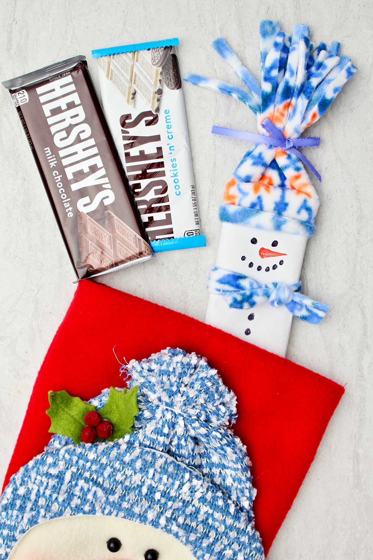 Completed candy bar snowman stocking stuffer with two other Hershey bars near a snowman decoration.