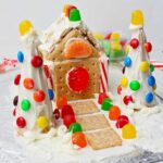 Completed gingerbread house using a milk carton decorated with colorful candies, white frosting, graham crackers, cereal and crackers.