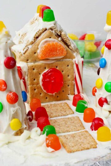 Completed gingerbread house using a milk carton decorated with colorful candies, white frosting, graham crackers, cereal and crackers.