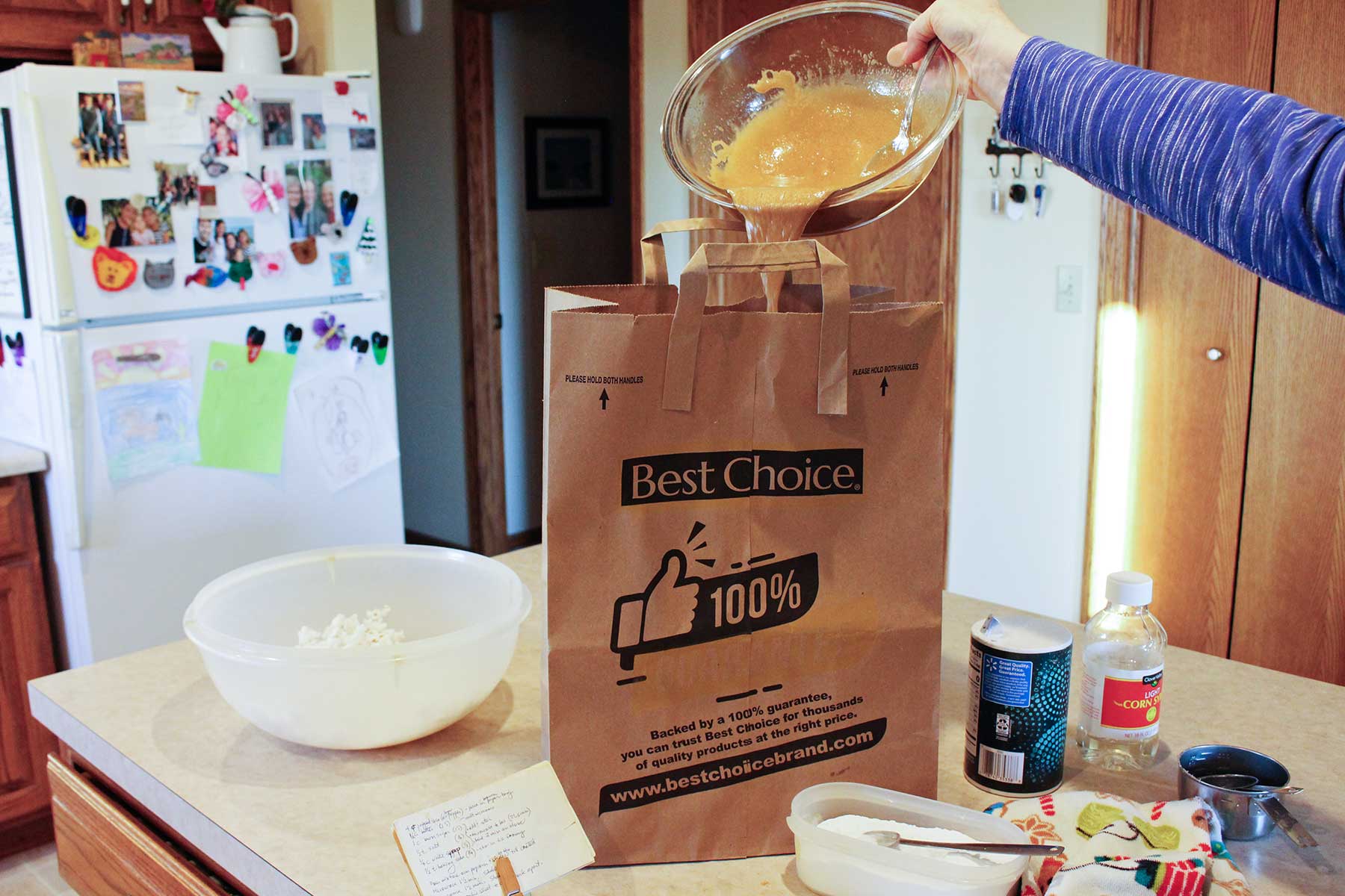 Person pouring caramel from a bowl into a paper bag on a kitchen counter.