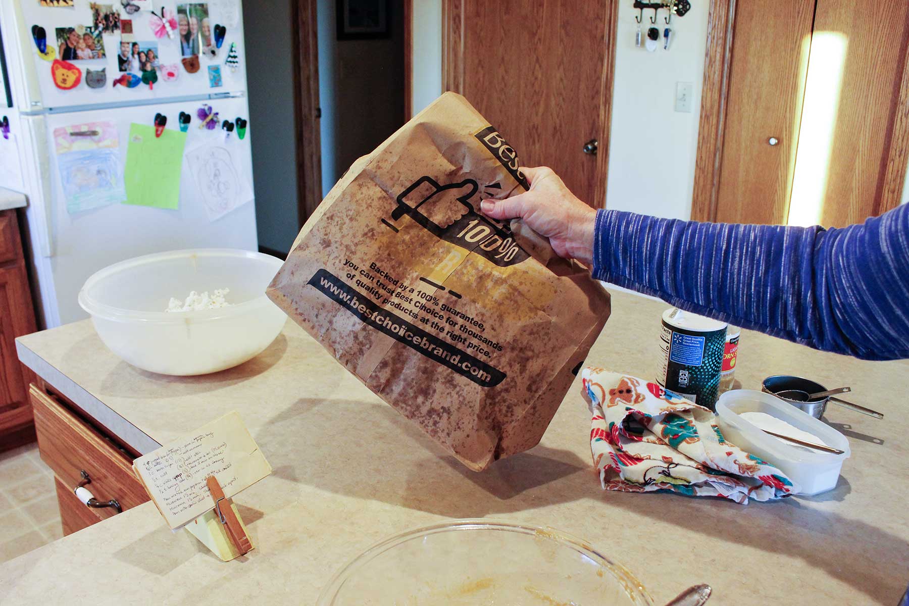 Person shaking closed paper bag with popcorn and caramel inside while at a kitchen counter.