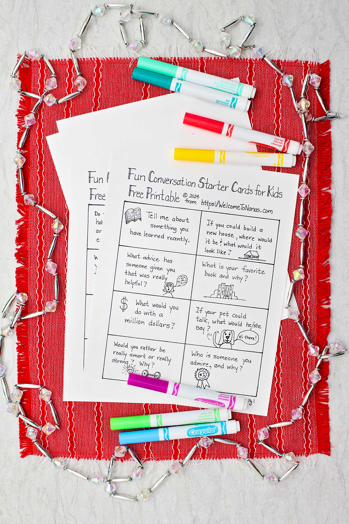 Fun conversation starter card printout sitting on a red placemat with colorful markers and crystal garland surrounding it.