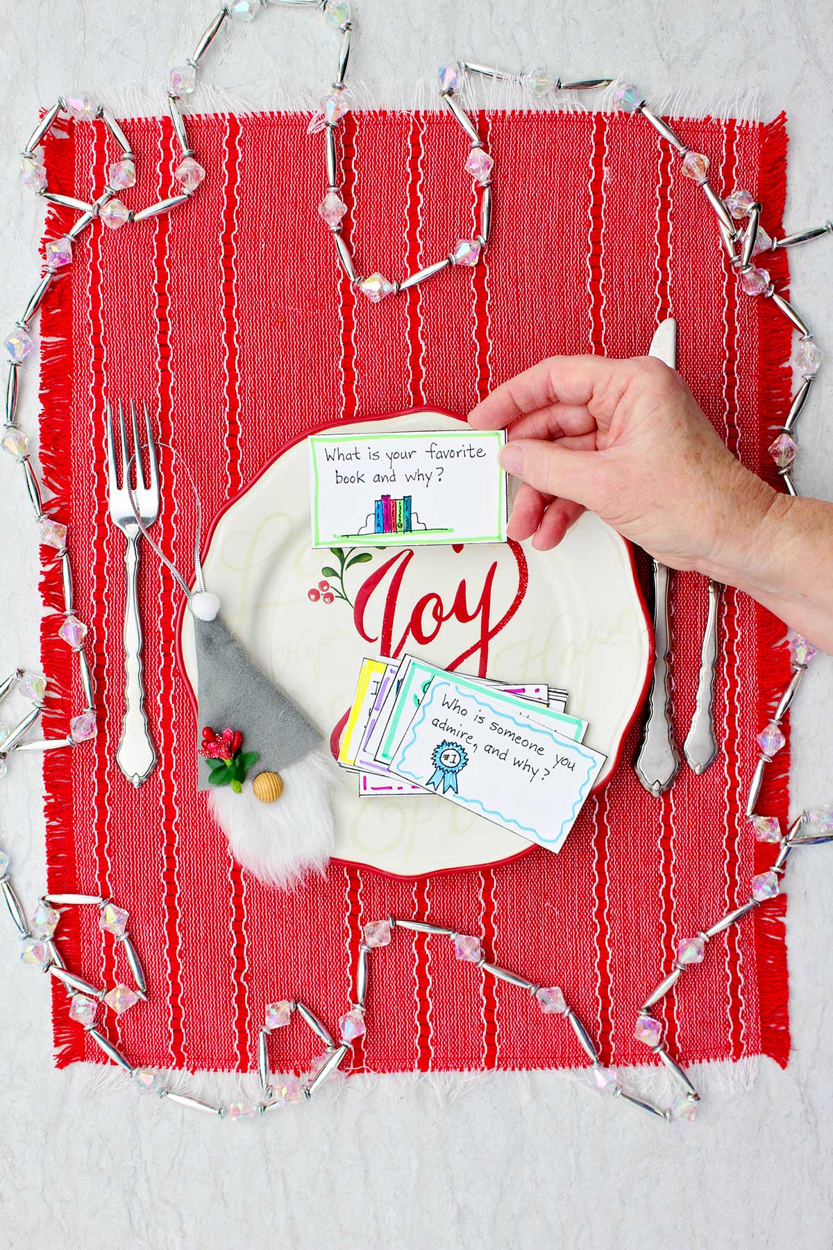 Person holding conversation starter card over a festive holiday plate on a red placemat.