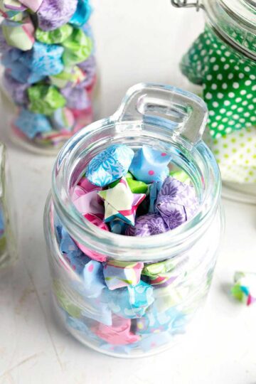 Colorful folded paper stars made from origami or scrapbook paper, added to glass jars