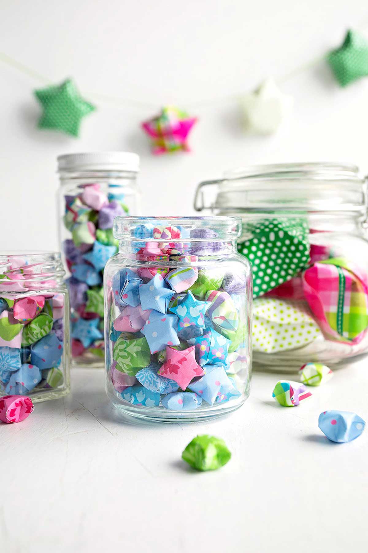 Colorful folded paper stars made from origami or scrapbook paper, added to glass jars