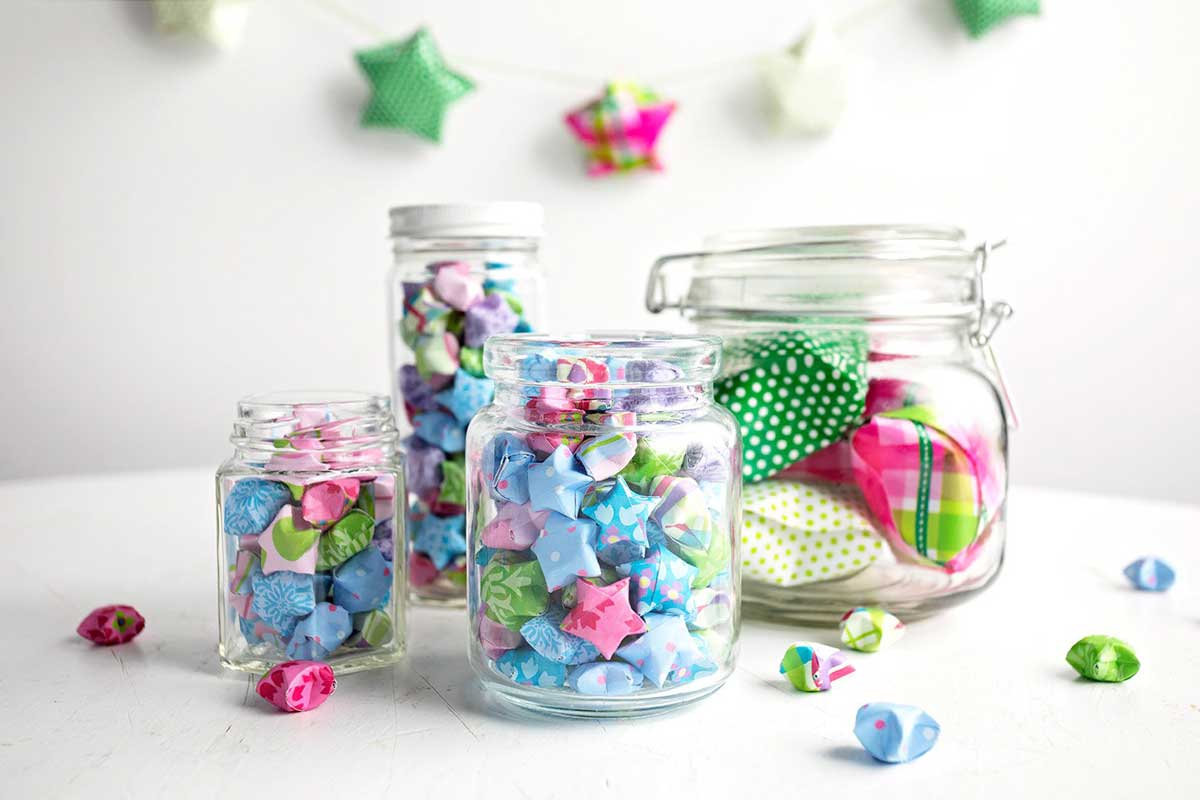 Colorful folded paper stars made from origami or scrapbook paper, added to glass jars