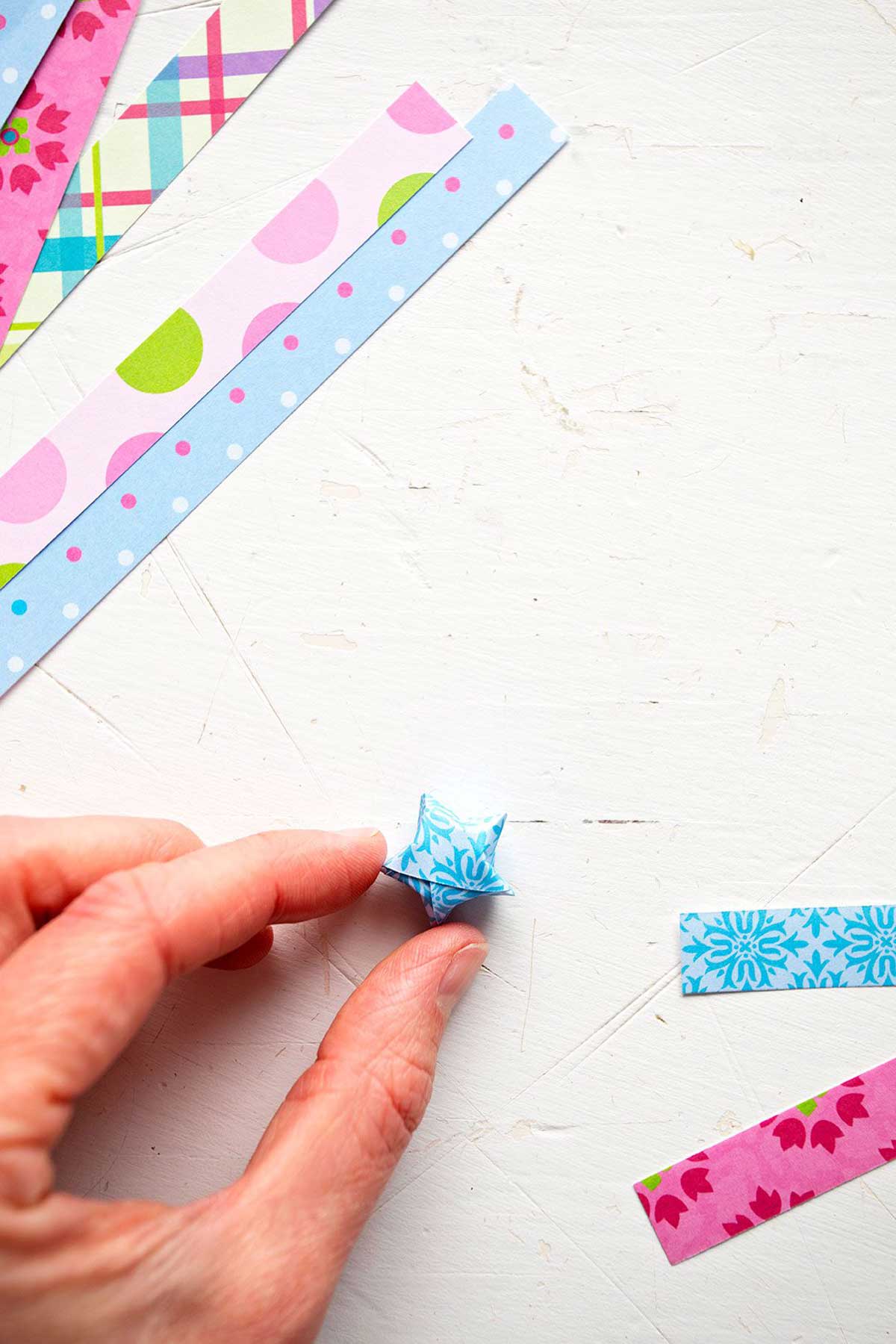 A final lucky paper star folded from blue scrapbook paper surrounded by strips of colorful thin paper