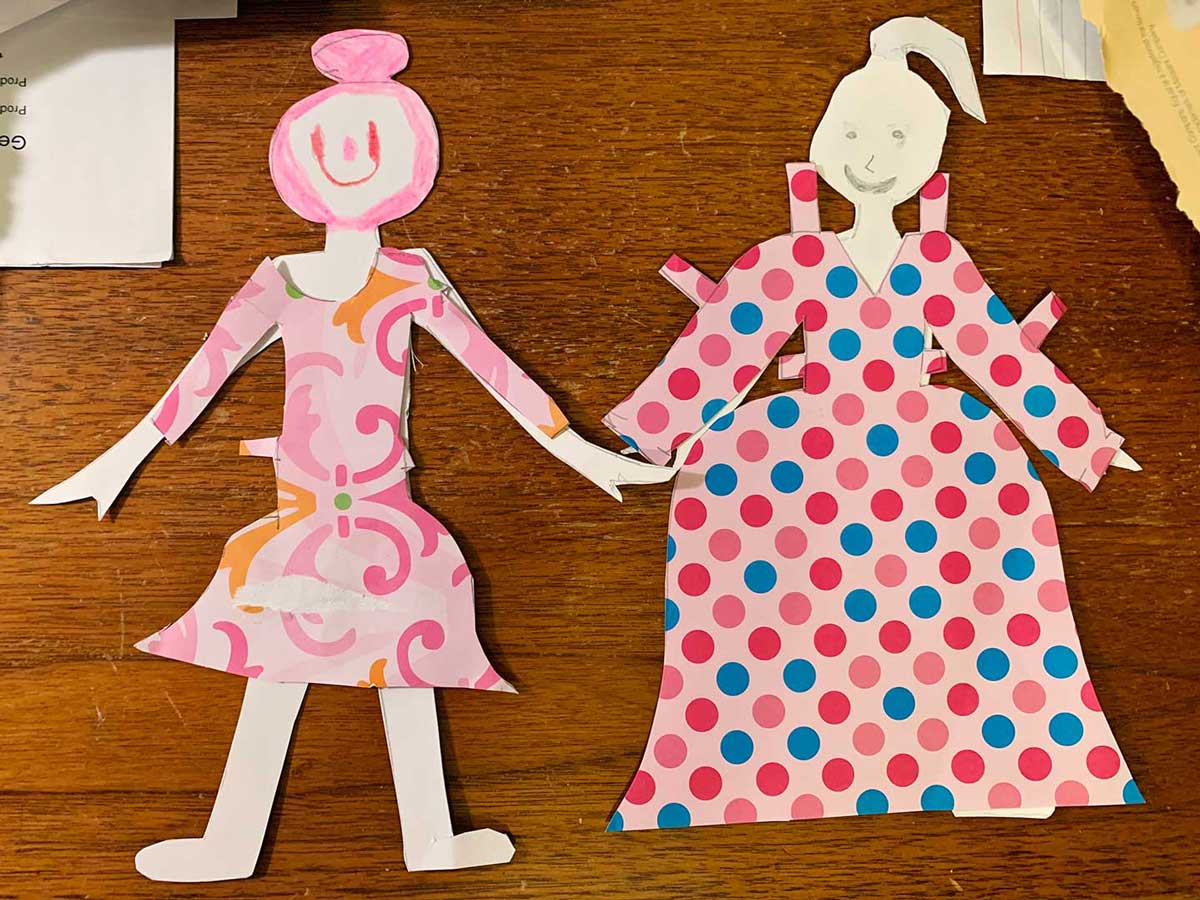 Two completed paper dolls with pink patterned dresses and hand drawn faces.