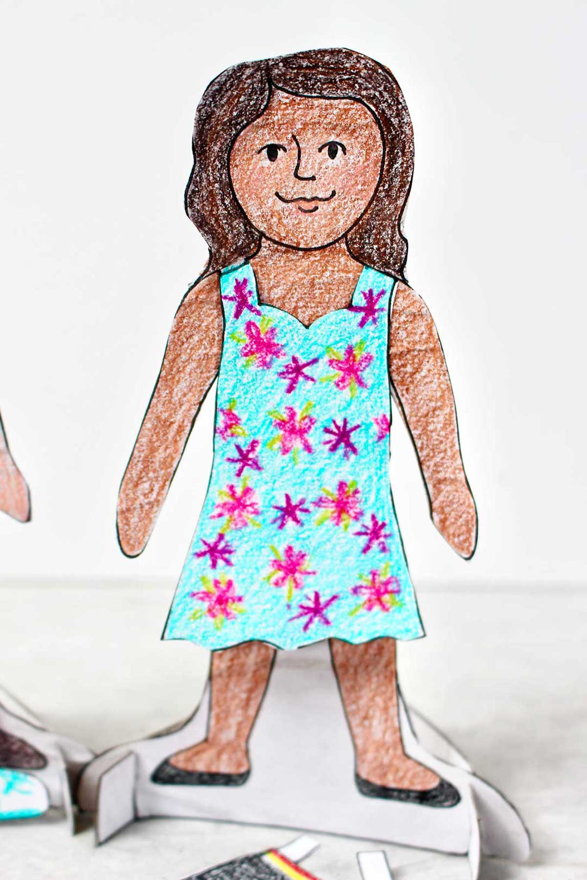 Girl paper doll with brown hair dressed in blue dress with pink stars on stand.