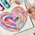 Hand painting finishing touches on completed abstract heart painting with paint supplies near by.
