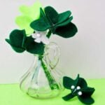 Kelly green and neon green felt shamrocks in a glass vase sitting on a green background.