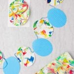Easter egg bunting made with blue striped paper eggs and marbled paper eggs on a blue ribbon with other pieces of marbled paper near by.