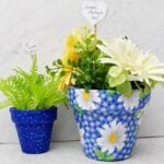 Completed decoupage flower pots with fabric filled with spring flowers and greenery.