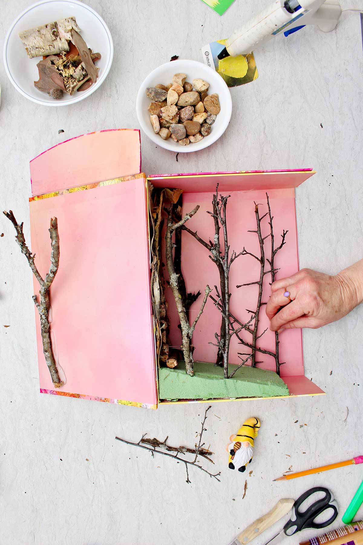 Person attaching twigs in the inside of a cut out gift box for the base of the miniature forest book nook.