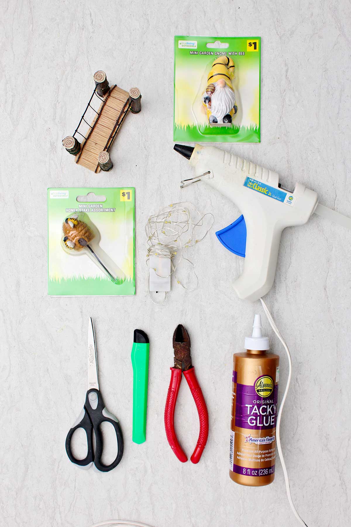 Glue gun, gnome statue, small bridge and honeycomb replicas, fairy lights, tacky glue and tools to make a miniature forest book nook shelf insert.